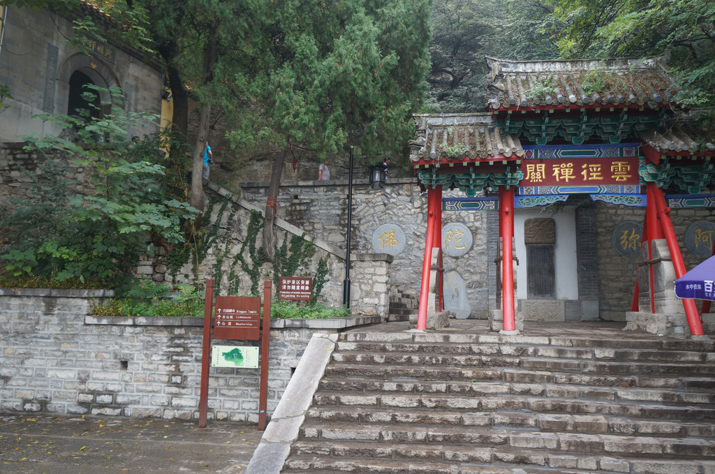 我们继续朝着略有迷雾的千佛山顶部前行,登山的台阶开始变窄,但整个步道打扫的还是非常干净。随后走过的是观音园,要另外购票5元/人才能进入参拜,冷清的园子内似乎鲜有人气问津。再往前走,在半山腰有个唐槐亭,朴素的亭子虽然很不起眼,但旁边的槐树可是大有名堂,据说当年曾经是秦琼拴马之树。于是这棵古树和附近比较粗壮的松柏树也都挂满了红色的祈福布条,以此寄托着民众期盼平安和幸福的愿望,这些红色的布条在雨后天晴的郁郁葱葱之中更加鲜艳夺目。 再往上走则看到途中一座彩色牌坊,上书齐烟九点,看了介绍才知道,原来古时在这